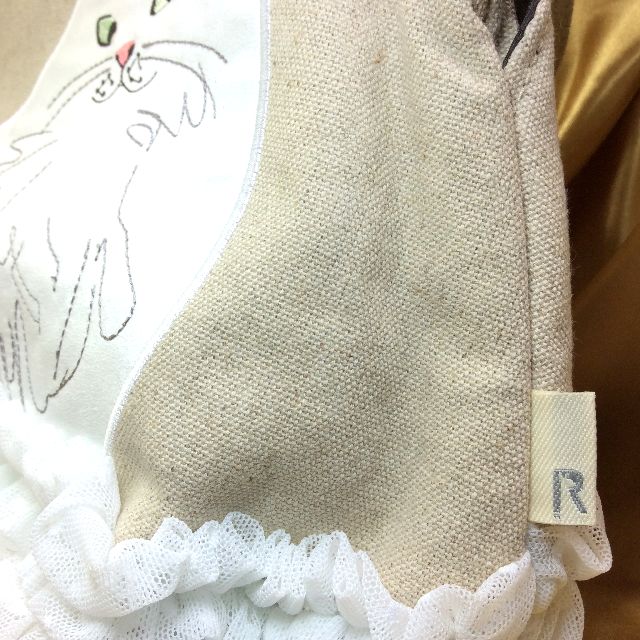 ルートートの白猫フリルがま口バッグの外側の脇のロゴマークタグとフリルの画像